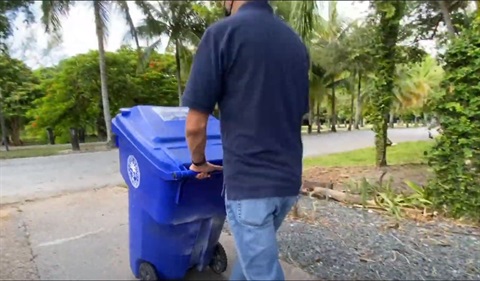 man rolls recycling bin to curb.JPG